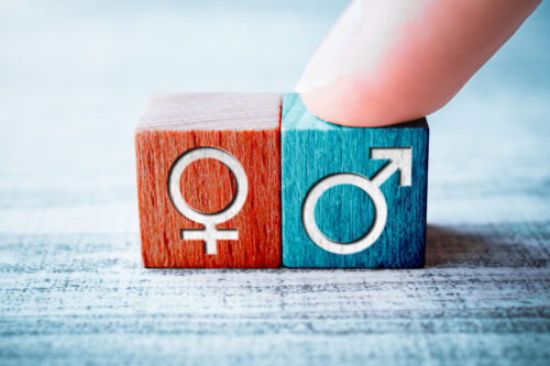Gender Icon For Male On A Wooden Block Arranged By One Finger Next To The Female Sign On A Table